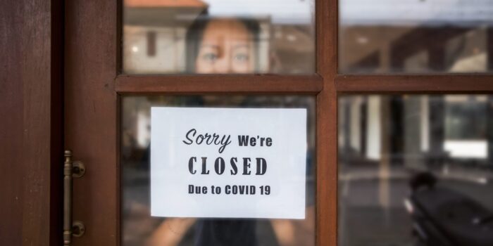 Portrait shot of business owner putting a closing down poster into a front door window during Covid 19 pandemic