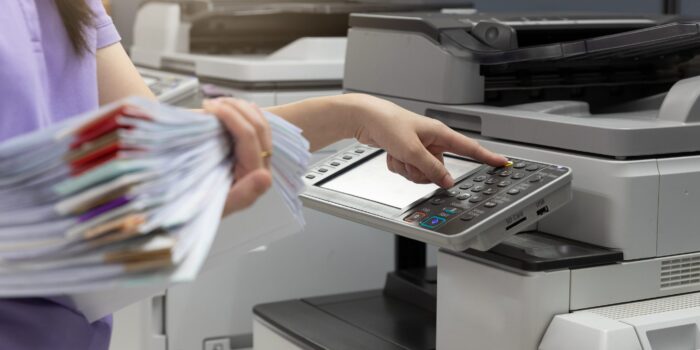 Bussinesswoman using copier machine to copy heap of paperwork in office.