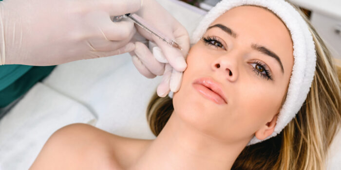 The doctor cosmetologist makes the Rejuvenating facial injections procedure for tightening and smoothing wrinkles on the face skin of a beautiful, young woman in a beauty salon. The hands of cosmetologist are close-ups that inject hyaluronic acid into the cheekbone area of the woman.