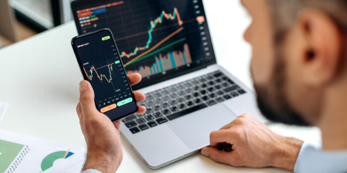 Trader investor analyst using mobile phone app for cryptocurrency stock market, analyzing graph trading data index investment growth chart, plans strategy. Close-up of male hands holding smartphone